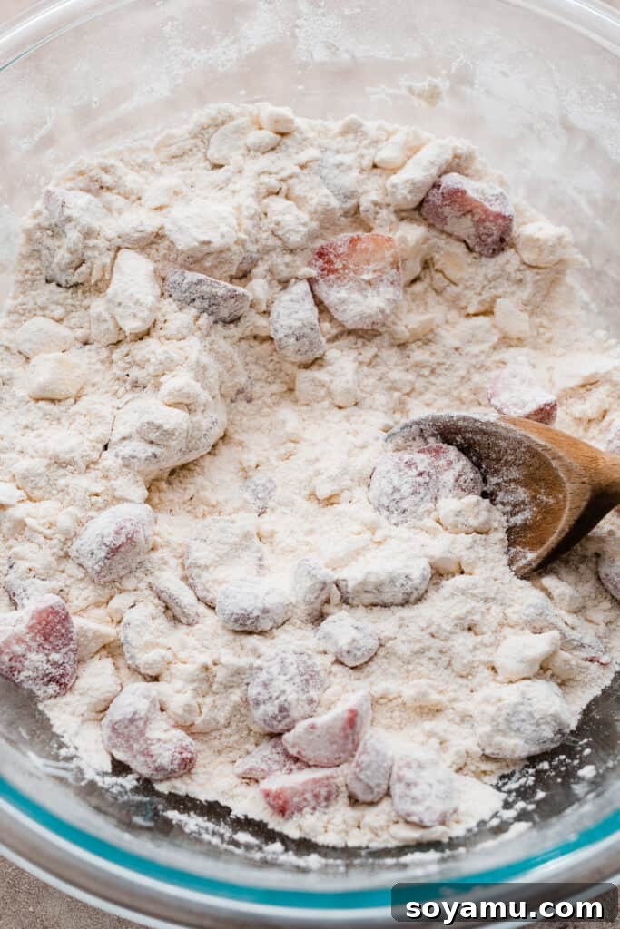 Strawberry Scones - A quick and delicious recipe that's buttery, flaky, sweet, and oh so delicious! Perfect for brunch, snacking, or enjoying all summer long! #strawberry #scones #strawberryscones #brunchrecipes #breakfastrecipes #sconerecipe #summerrecipes #baking #bluebowlrecipes | bluebowlrecipes.com A large bowl containing the dry ingredients, chunks of cold butter cut into the flour, and fresh strawberries coated in flour, ready for the wet ingredients.