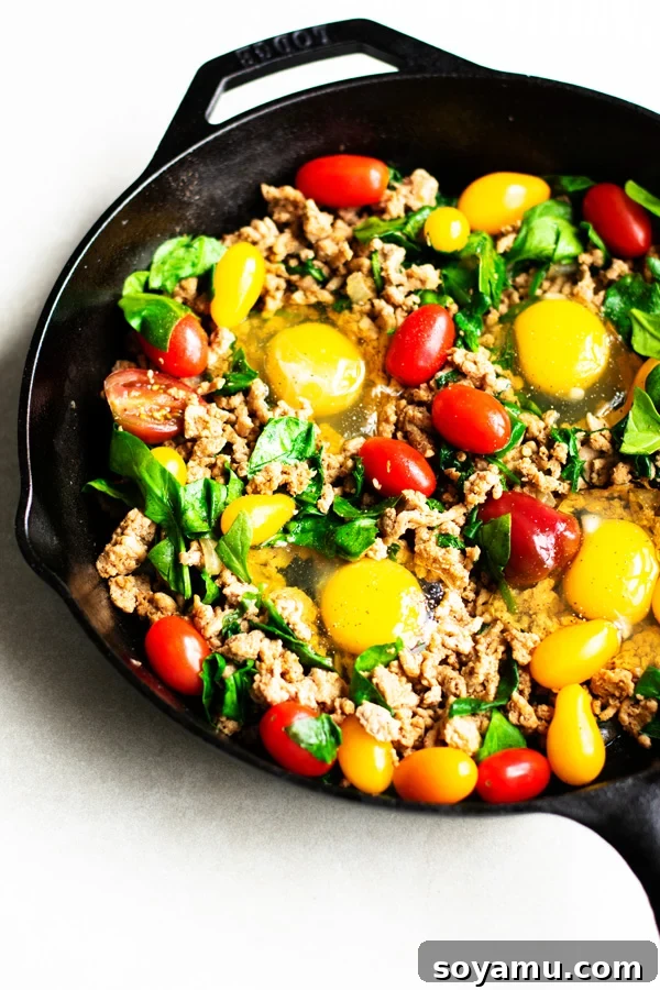 Healthy Taco Skillet cooking in a cast iron pan, showing raw eggs placed into the mixture before baking