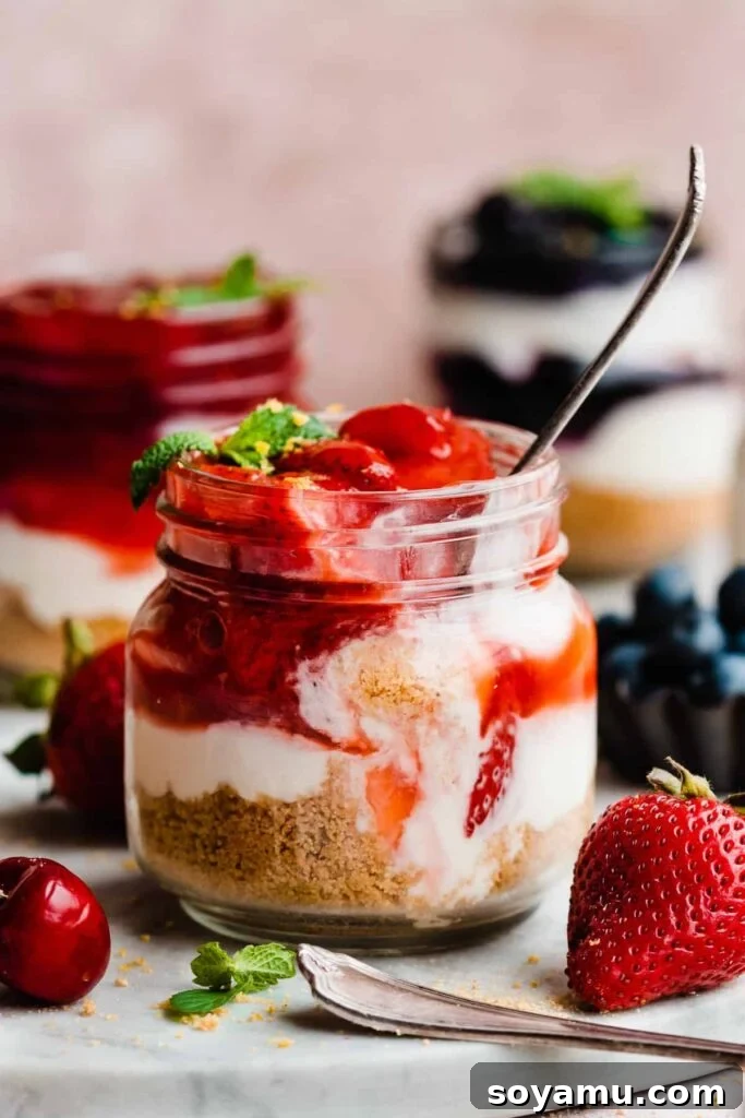 No-Bake Mini Cheesecake Jars 2 Jars of mini cheesecakes, with a spoon digging into the strawberry topped cheesecake.