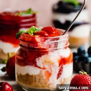 A close-up of a jar of mini cheesecake with strawberry topping, with a spoon digging in.