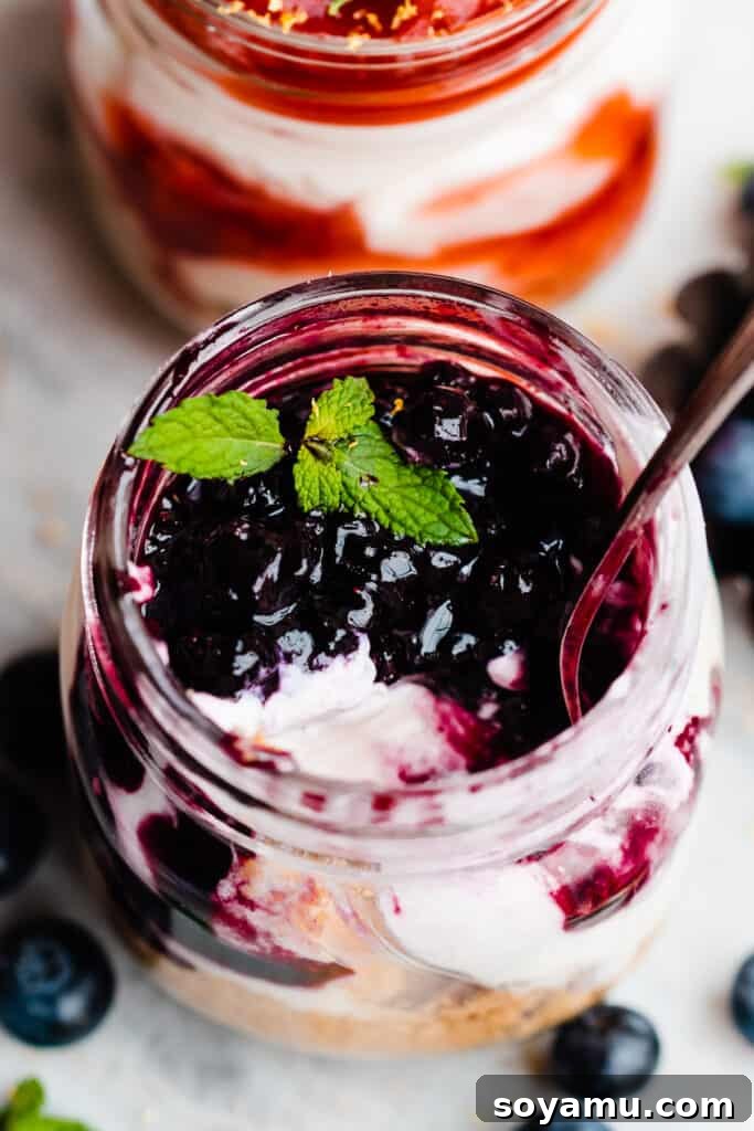No-Bake Mini Cheesecake Jars 8 A mini no-bake cheesecake topped with blueberry sauce, with a spoon digging in.