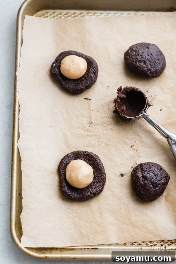 Raw chocolate cookie dough portioned and ready for baking, showcasing the perfect texture before stuffing with caramel. Balls of chocolate cookie dough prepared on a baking sheet, ready for the oven.