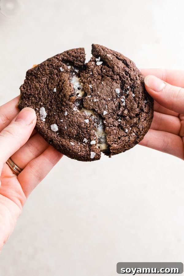 Stack of rich chocolate cookies with a visible caramel center, dusted with sea salt. Stacked Caramel-Stuffed Chocolate Cookies with a view of the gooey caramel inside.