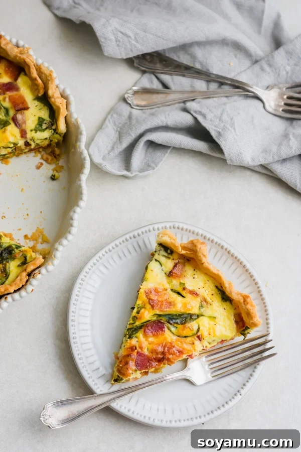 Perfect Breakfast Quiche - Our favorite Breakfast Quiche! The buttery flaky crust is filled with fluffy eggs, sharp cheddar cheese, spinach, and perfectly crispy bacon! #breakfastrecipes #easyrecipes #quiche #quicherecipes #baconrecipes #eggrecipes #mealideas | bluebowlrecipes.com A perfectly baked slice of breakfast quiche on a white plate, ready to be enjoyed.