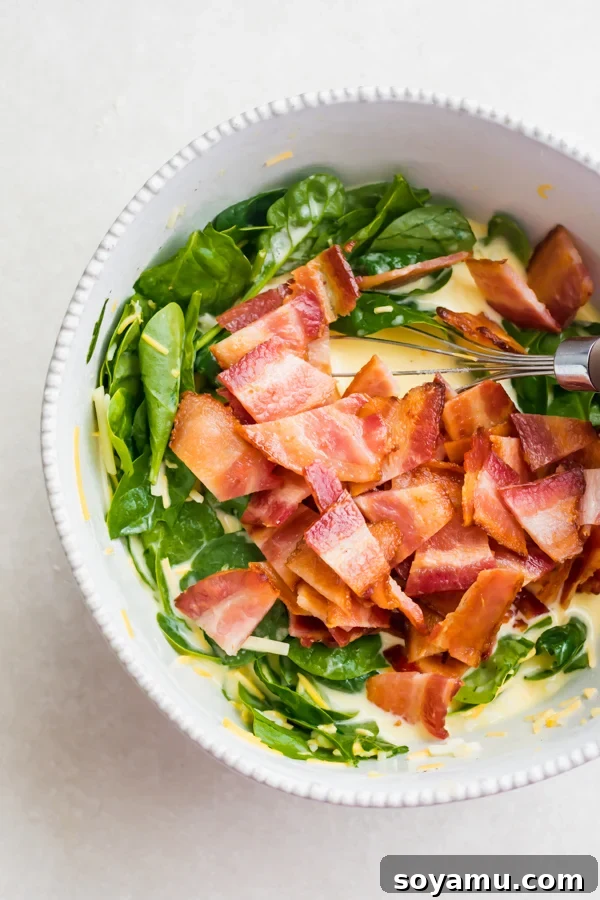 Perfect Breakfast Quiche - Our favorite Breakfast Quiche! The buttery flaky crust is filled with fluffy eggs, sharp cheddar cheese, spinach, and perfectly crispy bacon! #breakfastrecipes #easyrecipes #quiche #quicherecipes #baconrecipes #eggrecipes #mealideas | bluebowlrecipes.com A bowl filled with the colorful breakfast quiche filling, showing eggs, bacon, spinach, and cheese mixed together.
