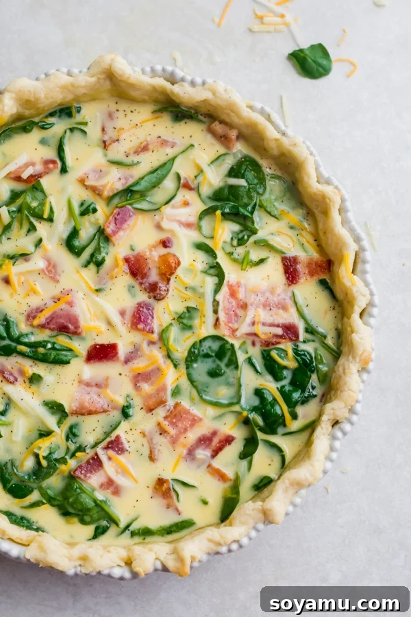 Perfect Breakfast Quiche - Our favorite Breakfast Quiche! The buttery flaky crust is filled with fluffy eggs, sharp cheddar cheese, spinach, and perfectly crispy bacon! #breakfastrecipes #easyrecipes #quiche #quicherecipes #baconrecipes #eggrecipes #mealideas | bluebowlrecipes.com The quiche filling poured into the par-baked pie crust, ready for baking.