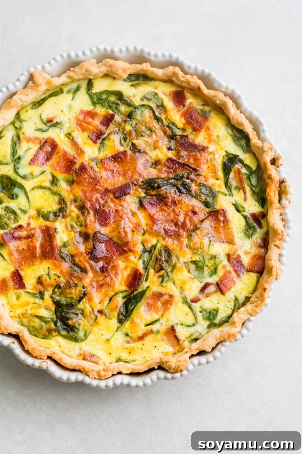 Perfect Breakfast Quiche - Our favorite Breakfast Quiche! The buttery flaky crust is filled with fluffy eggs, sharp cheddar cheese, spinach, and perfectly crispy bacon! #breakfastrecipes #easyrecipes #quiche #quicherecipes #baconrecipes #eggrecipes #mealideas | bluebowlrecipes.com A fully baked breakfast quiche with a golden crust and bubbly, set filling, straight from the oven.