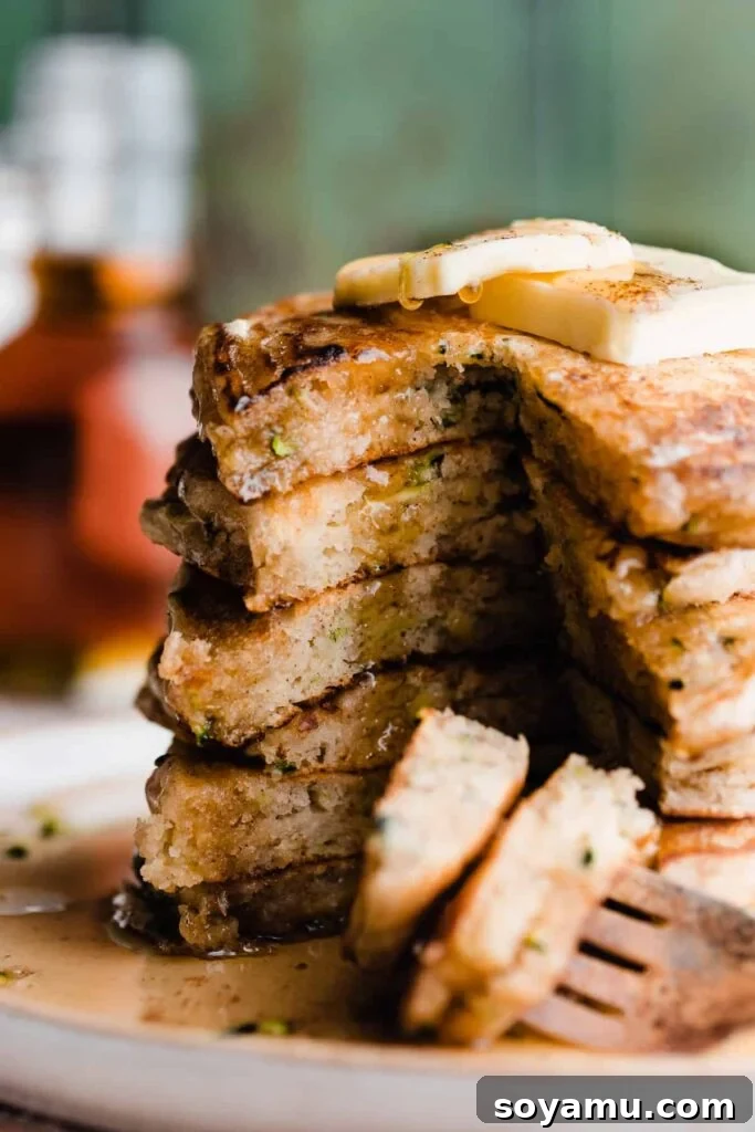 Spiced Zucchini Pancakes 2 A stack of sliced open zucchini pancakes with maple syrup dripping down, garnished with a pat of butter.