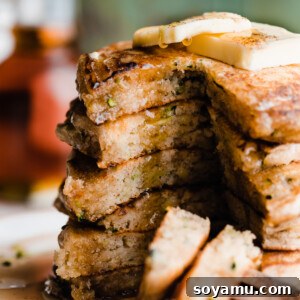 A stack of sliced open zucchini pancakes with maple syrup dripping down.