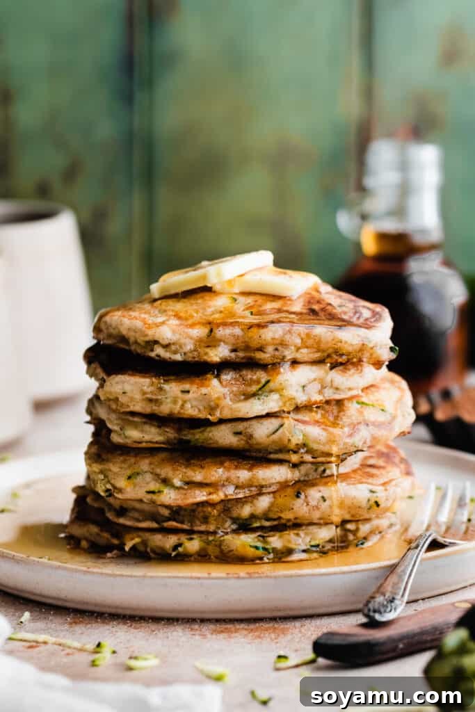 Spiced Zucchini Pancakes 7 A stack of zucchini pancakes dripping with maple syrup and a pat of butter, ready to be enjoyed.