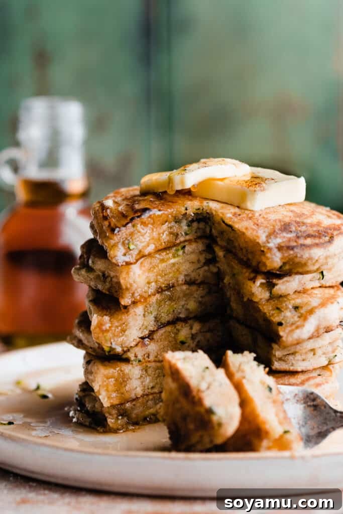 Spiced Zucchini Pancakes 8 A close-up of a stack of zucchini pancakes, sliced open to reveal the moist interior, with butter and syrup on top.