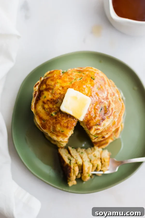 Spiced Zucchini Pancakes 9 A top-down view of a generous stack of golden Zucchini Bread Pancakes, garnished with butter and maple syrup.