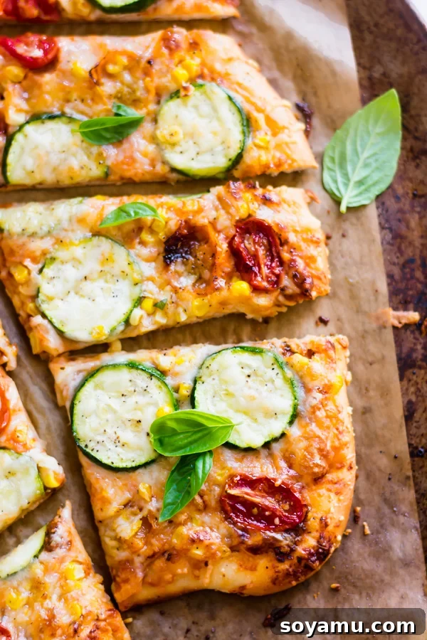 An enticing slice of Roasted Tomato, Corn, and Zucchini Flatbread Pizza, showing its bubbly cheese and colorful roasted vegetables.