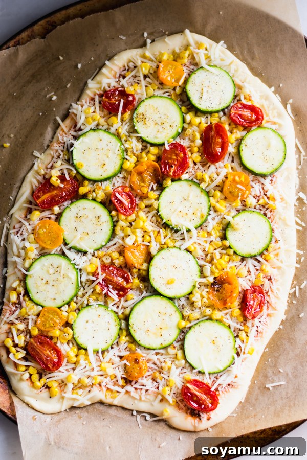 Unbaked flatbread pizza, topped with sauce, cheese, roasted tomatoes, corn, and zucchini, ready for the oven.