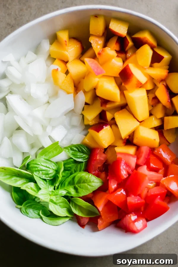 Freshly chopped peaches, red onions, tomatoes, and green basil in a mixing bowl.
