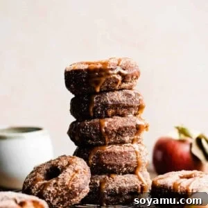 A stack of apple cider donuts coated in apple pie spice sugar and dripping in caramel sauce.
