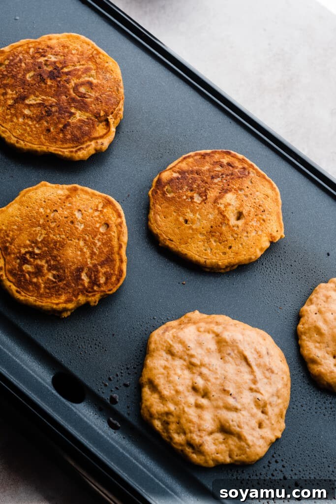 Pillowy Pumpkin Spice Pancakes 5 Several pumpkin pancakes cooking on a hot griddle, with some already golden brown.