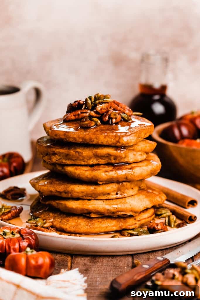 Pillowy Pumpkin Spice Pancakes 7 A tall stack of fluffy pumpkin pancakes generously topped with candied pecans and dripping with maple syrup.