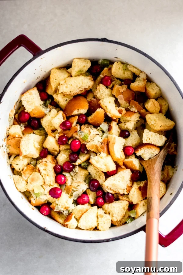 Combining Stuffing Ingredients Cooked aromatics and dried brioche bread cubes being combined in a large pot with chicken broth, ready to be mixed for stuffing.