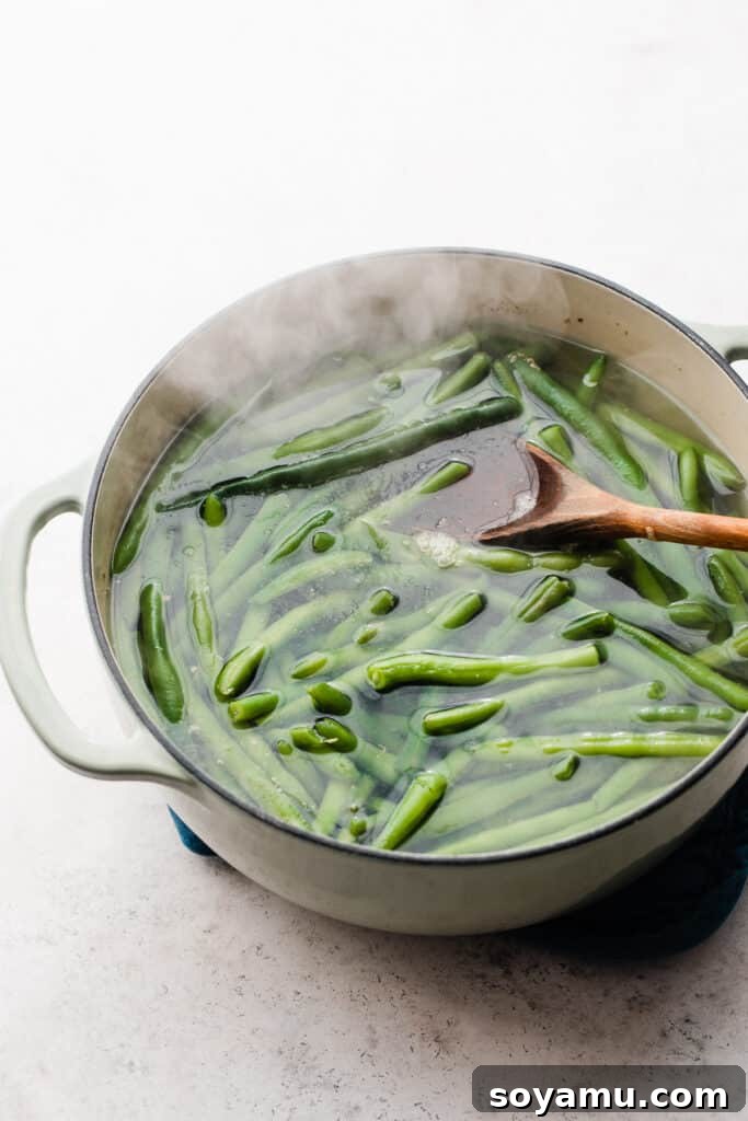 Effortless Gluten-Free Dairy-Free Bacon Green Beans 5 A dutch oven filled with steaming water and green beans.