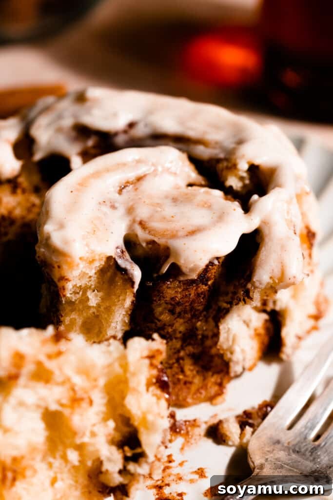 A close-up of a partially unwound cinnamon roll, revealing the soft, layered brioche dough and generous cinnamon swirl.