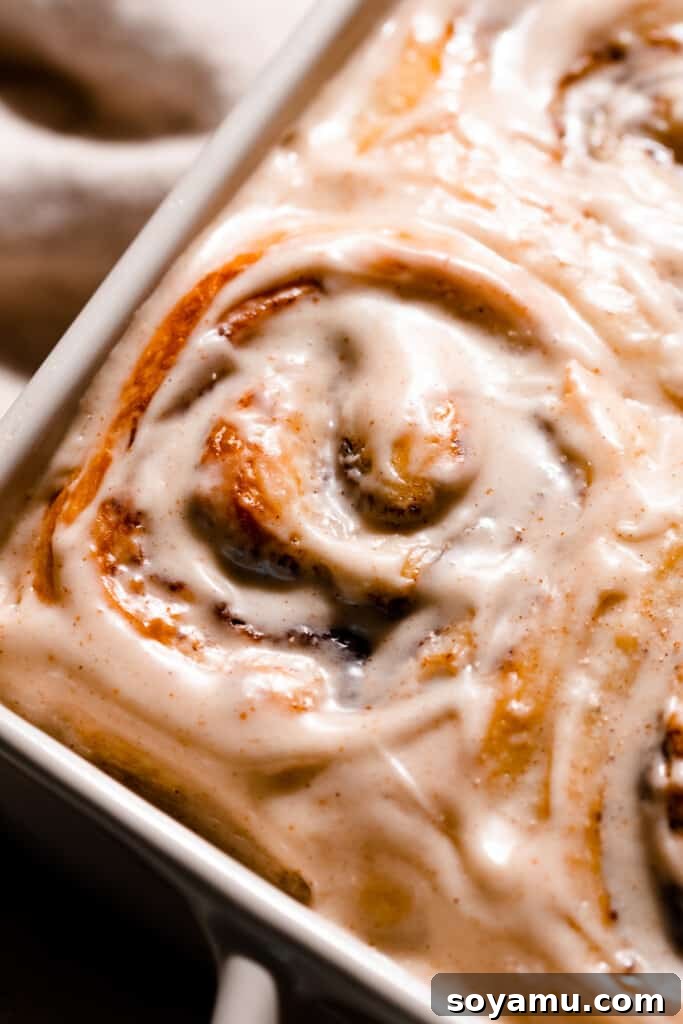 A close-up of a generously frosted brioche cinnamon roll, showcasing its soft texture and rich icing.