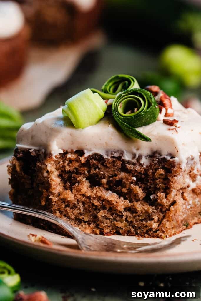 Irresistible Zucchini Snack Cake with Brown Butter Cream Cheese Frosting 10 A close-up shot of a single slice of zucchini cake, perfectly frosted and with a small bite missing, resting on a white plate, highlighting its appetizing appeal.