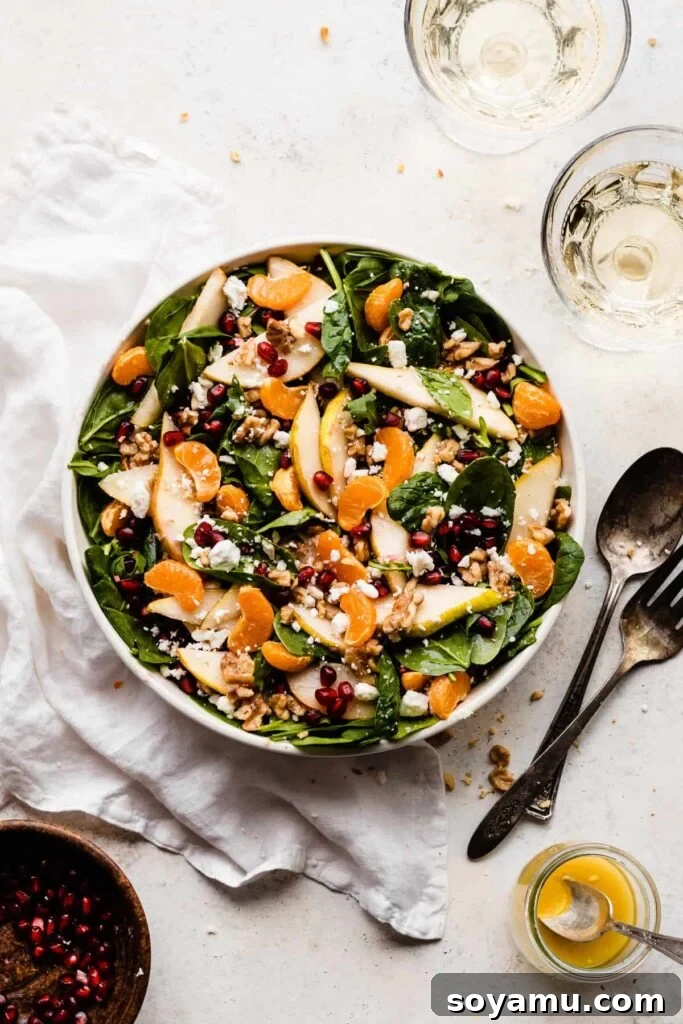 Jeweled Winter Pear Pomegranate Walnut Salad 2 A beautifully tossed winter salad featuring vibrant green leaves, glistening pomegranate seeds, thinly sliced pears, bright clementine segments, crunchy walnuts, and crumbled feta cheese, ready to be served.