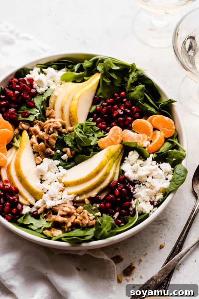 Jeweled Winter Pear Pomegranate Walnut Salad 3 A closer view of the winter salad ingredients: fresh greens, thinly sliced pears, bright red pomegranate seeds, orange segments, crunchy walnuts, and creamy feta cheese in a serving bowl.
