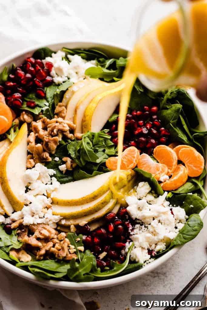 Jeweled Winter Pear Pomegranate Walnut Salad 4 Close-up of a hand pouring the golden honey vinaigrette dressing over a bowl of fresh winter salad ingredients.