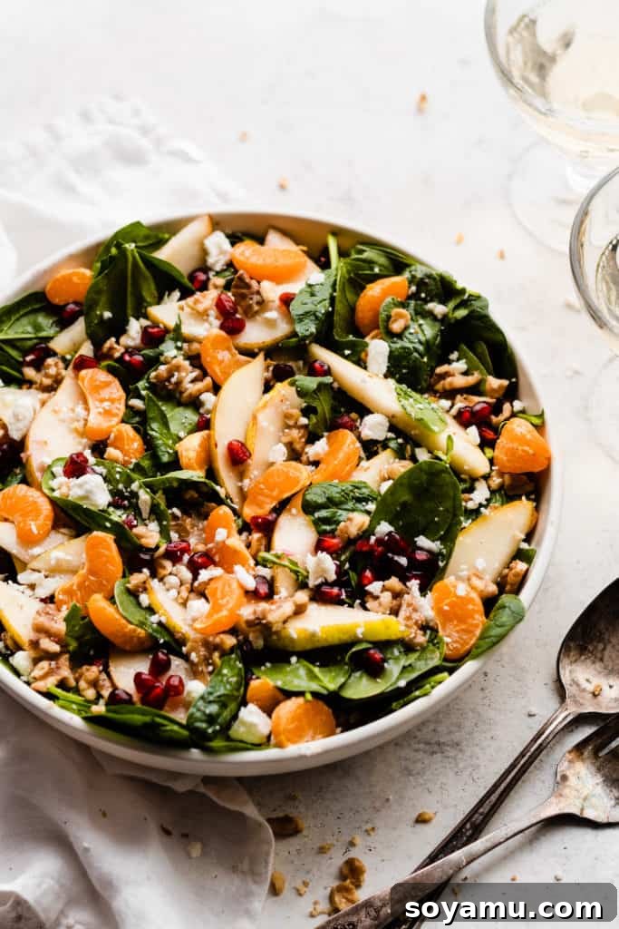 Jeweled Winter Pear Pomegranate Walnut Salad 5 A vibrant bowl of winter salad, fully tossed, featuring a colorful mix of greens, pear slices, clementine segments, glistening pomegranate seeds, walnuts, and crumbled feta cheese.