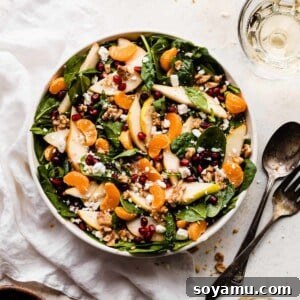 A salad bowl full of fresh greens, sliced pears, pomegranates, mandarin oranges, and walnuts, perfectly dressed and ready to be enjoyed.