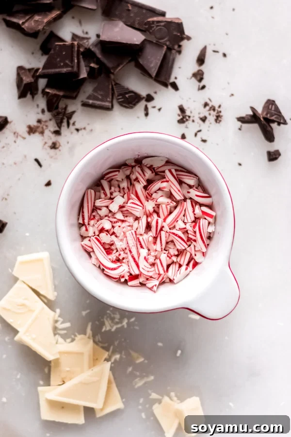 Chocolate Covered Peppermint Pretzels - A quick and festive recipe that will brighten up any holiday cookie plate! All you need is white chocolate, milk chocolate, pretzels, and crushed candy canes! #peppermint #chocolate #chocolatepretzel #christmas #holidayrecipes #nobake #christmasdessert #bluebowlrecipes Close-up of vibrant crushed candy canes alongside bowls of melted chocolate, perfectly prepared for dipping pretzels.