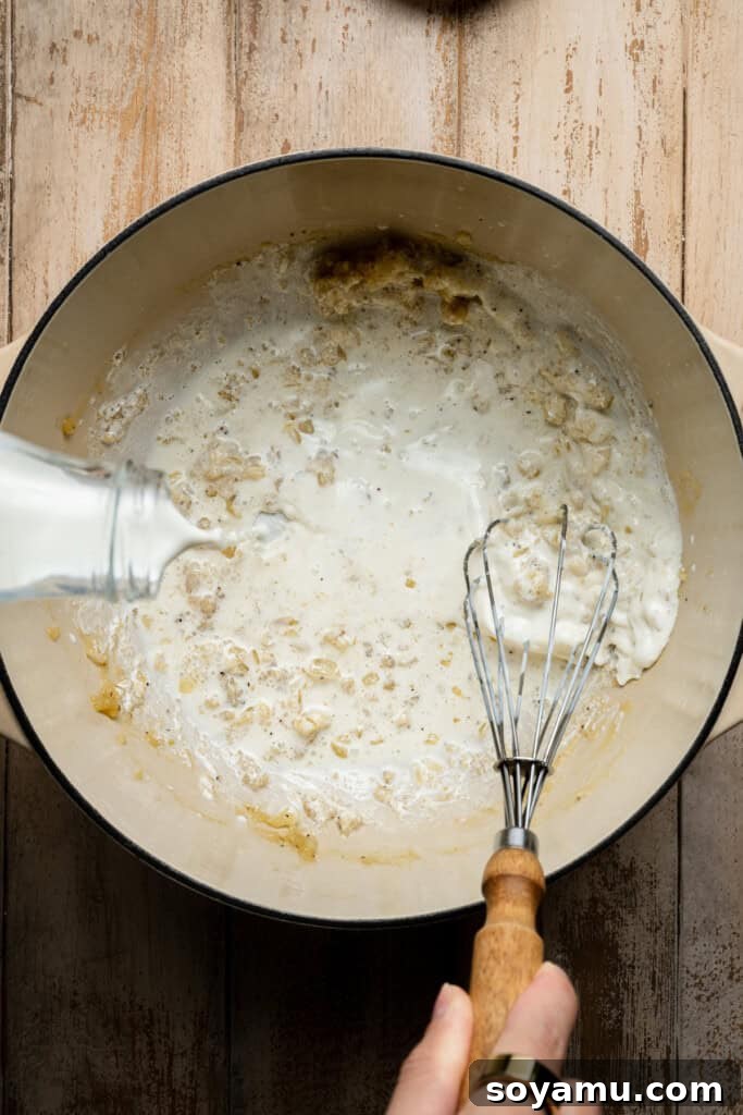 Rich half and half being slowly poured into the soup base, transforming it into a thick, creamy texture.