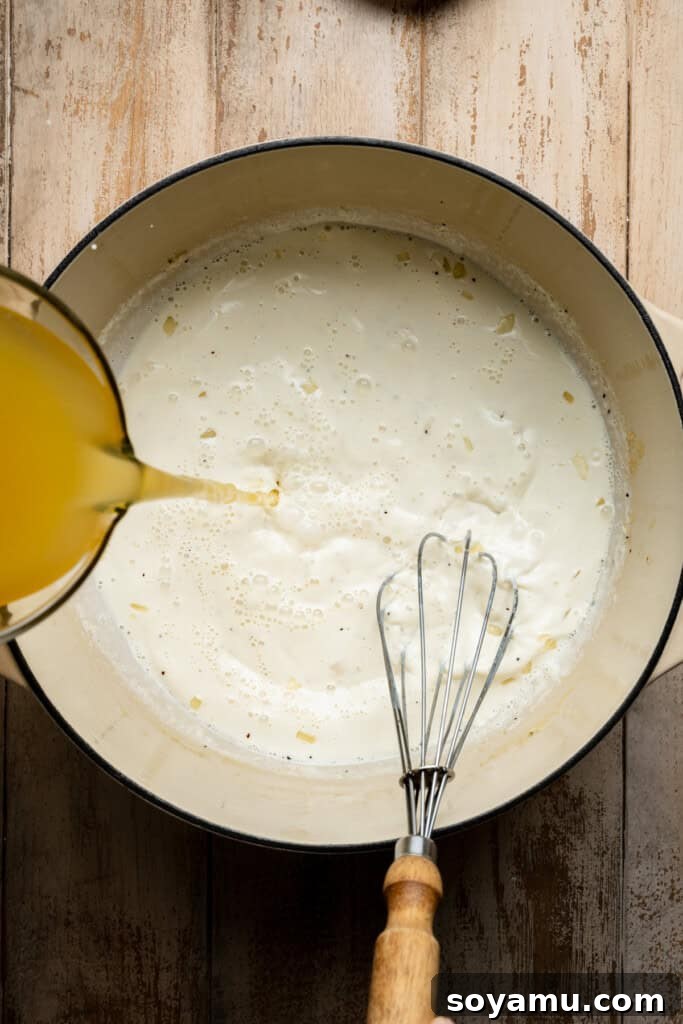 Savory chicken broth being poured into the creamy soup mixture, adding depth of flavor and thinning it slightly before simmering.