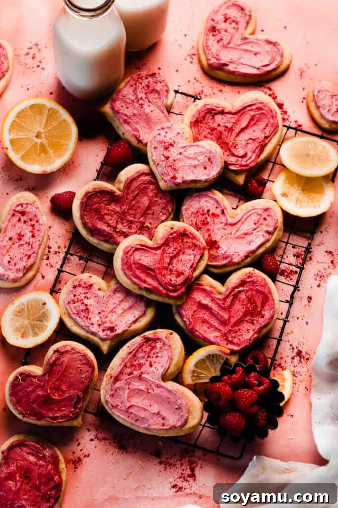 Heart shaped cutout cookies frosted in various shades of pink frosting, on a vintage wire rack, on a pink backdrop. 