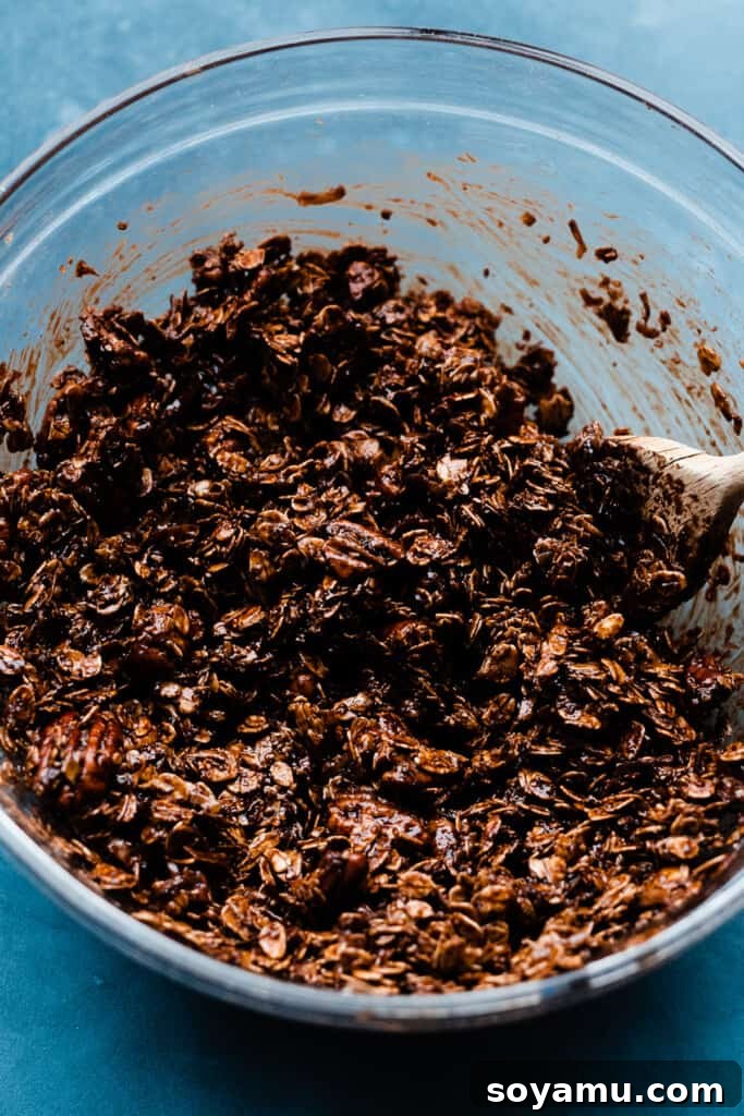 A bowl of the unbaked chocolate granola mixture, glistening with wet ingredients and ready to be spread on a pan.