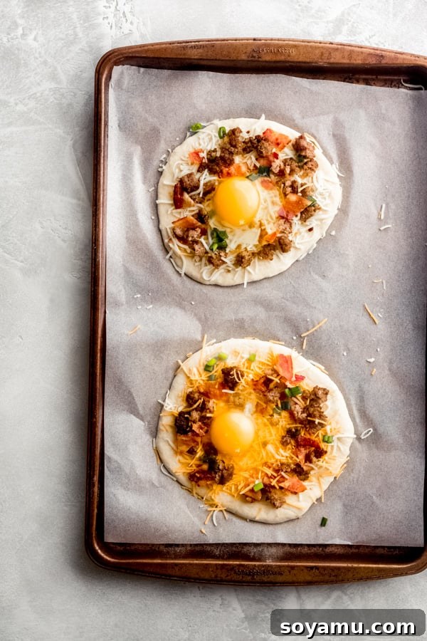 Assembled breakfast pizzas with eggs, prepared for baking to perfection. Breakfast pizzas on a baking tray with raw eggs cracked into the center of each pizza, ready for baking.