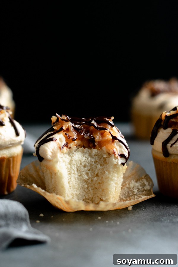 Close-up of a Samoa cupcake with a bite taken out, revealing the fluffy vanilla cake and layers of topping.