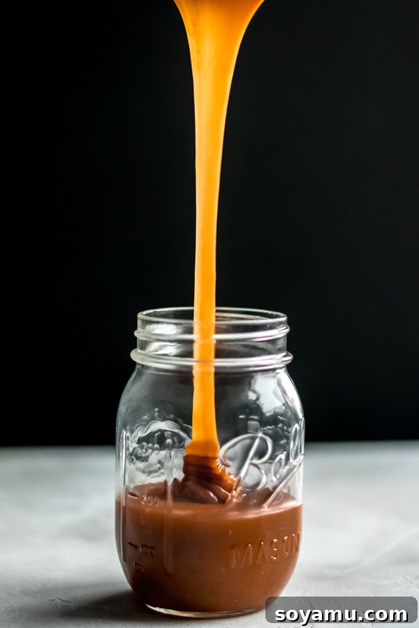 Golden homemade caramel sauce being poured into a clear glass jar.