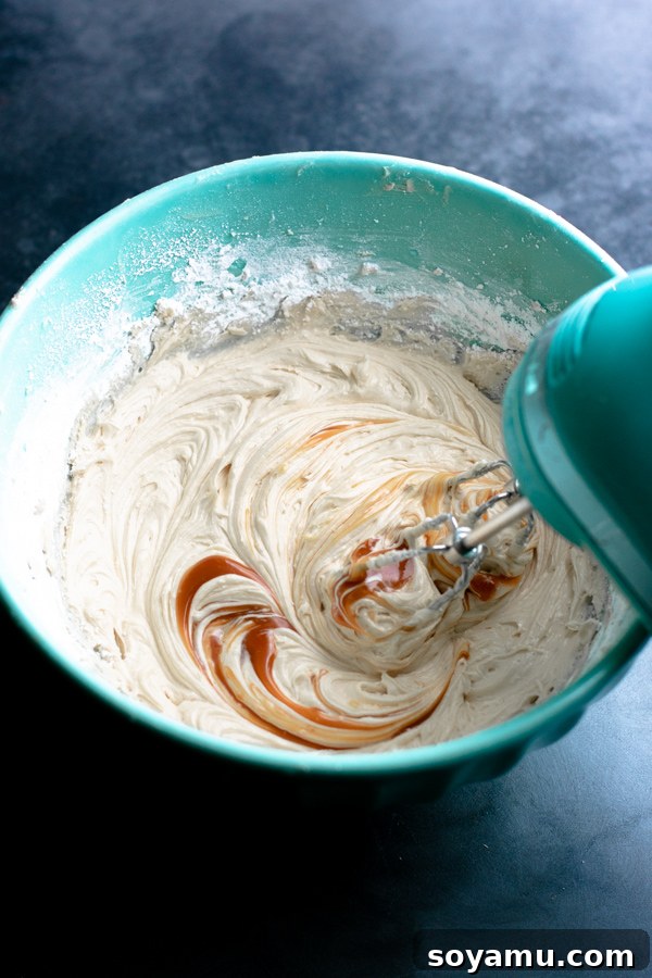 Caramel sauce being mixed into fluffy buttercream in a bowl, creating a smooth, luscious frosting.