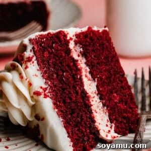 A slice of moist red velvet cake, frosted with cream cheese frosting, on a dessert plate.