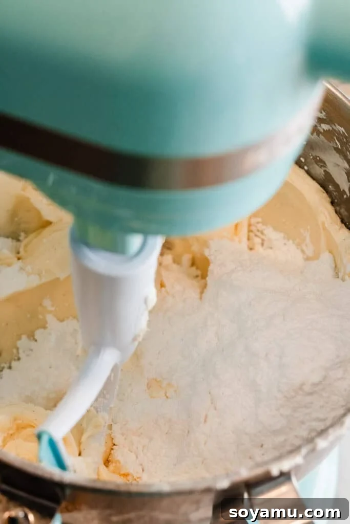 Silky Cream Cheese Frosting Perfection 6 Powdered sugar being carefully added to the creamy mixture of butter and cream cheese in a mixing bowl, illustrating the final steps of frosting preparation.