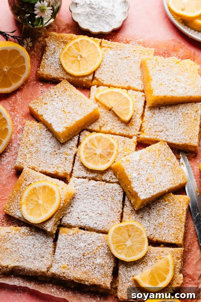 Effortless Zesty Lemon Bars 13 A collection of sliced lemon bars, beautifully dusted with powdered sugar, arranged on a charming pink surface, ready to be served.
