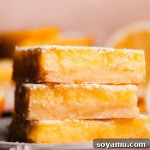 A stack of three luscious lemon bars on a plate, perfectly golden and dusted with powdered sugar.