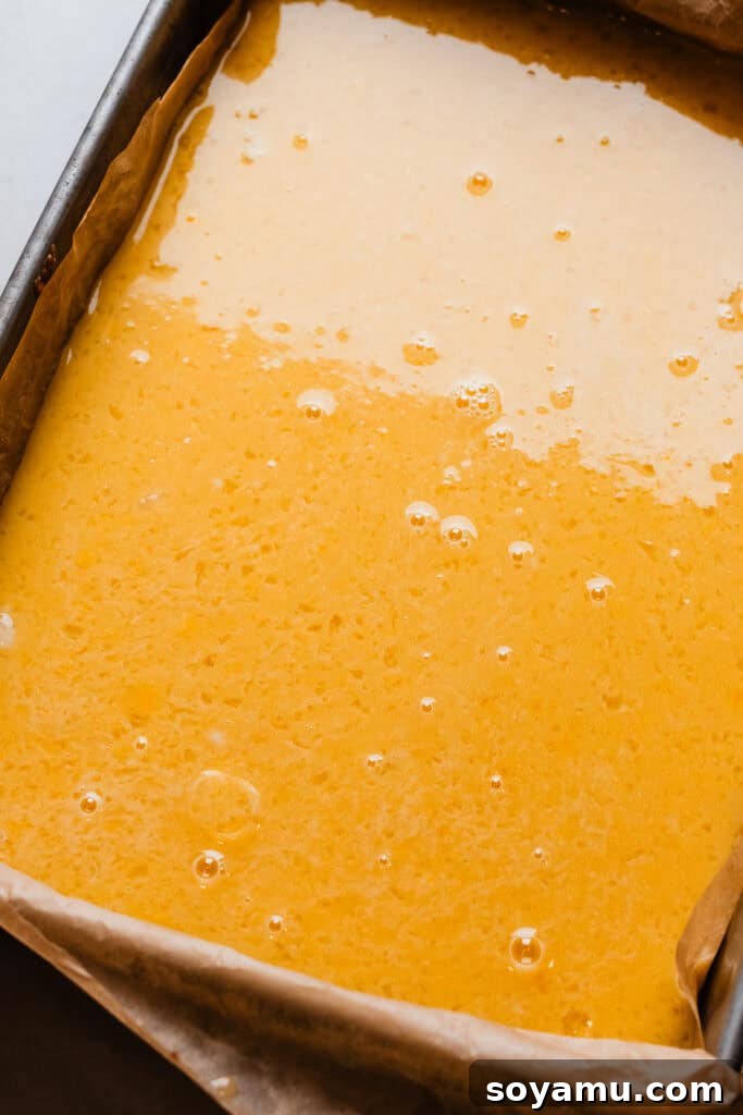 Effortless Zesty Lemon Bars 9 A baking pan filled with the partially baked shortbread crust and a layer of vibrant lemon filling poured over it, ready for the final bake.