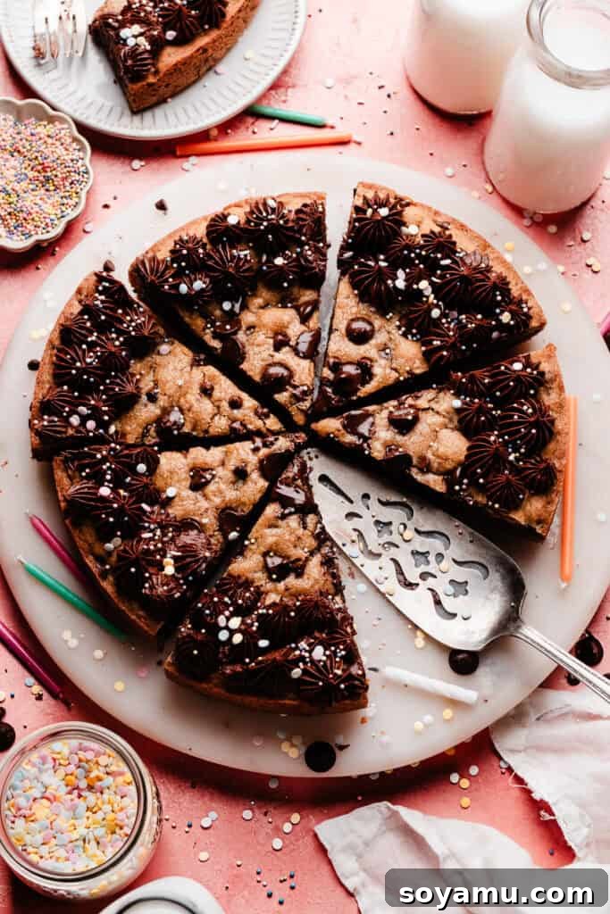 Chocolate Chip Cookie Cake Recipe — Soft, Chewy, Crowd-Pleasing 2 The sliced chocolate chip cookie cake on a marble plate, set on a pink backdrop. There are sprinkles and colorful birthday candles scattered around.