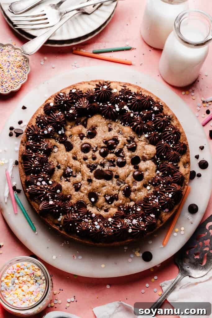 Chocolate Chip Cookie Cake Recipe — Soft, Chewy, Crowd-Pleasing 9 The baked chocolate chip cookie plate on a marble plate, decorated with chocolate fudge frosting and sprinkles.