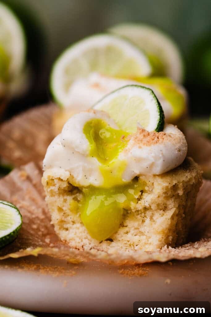 A close-up of a lime cupcake with a bite missing, showing the lime curd filling inside.