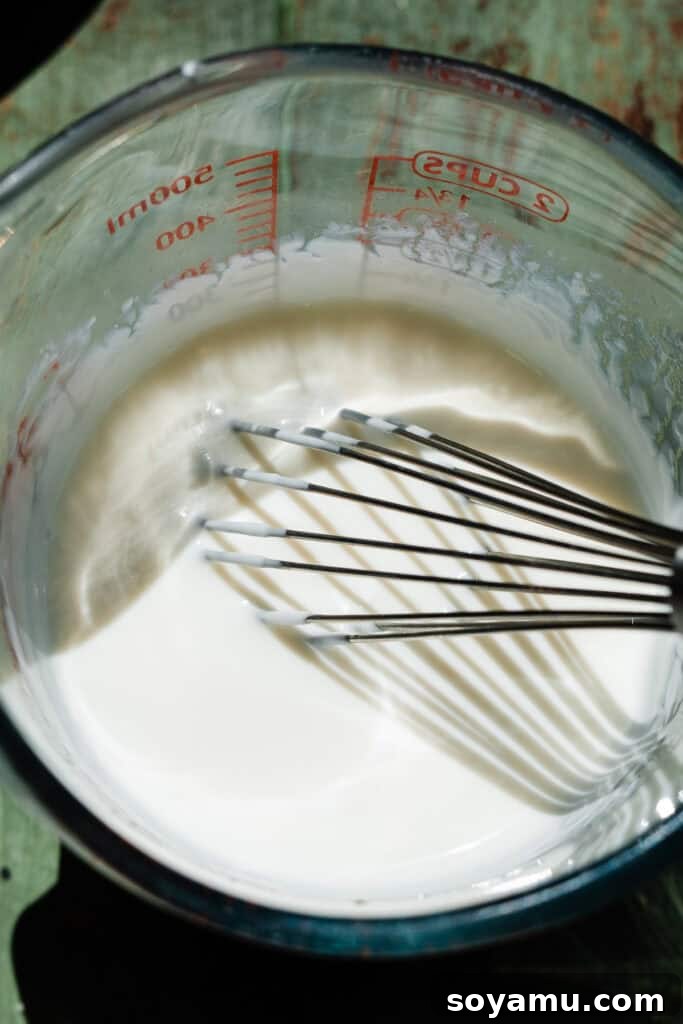 A glass measuring cup with the sour cream, milk, water, and vinegar whisked together.